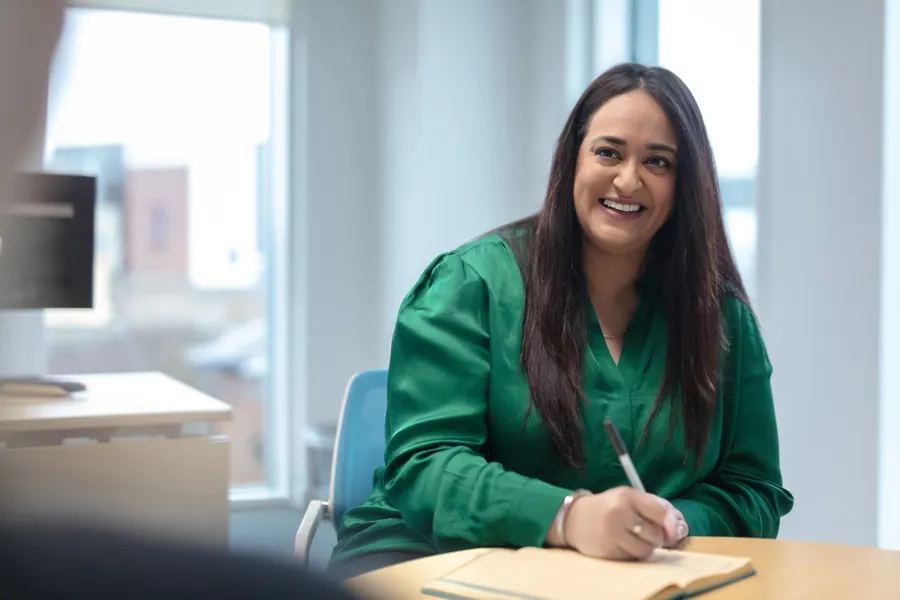 A woman in a green blouse smiles while taking notes at a desk