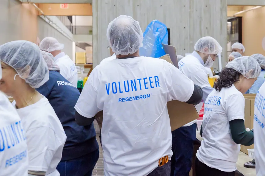 Volunteers wearing matching shirts and hairnets work together in a community service setting
